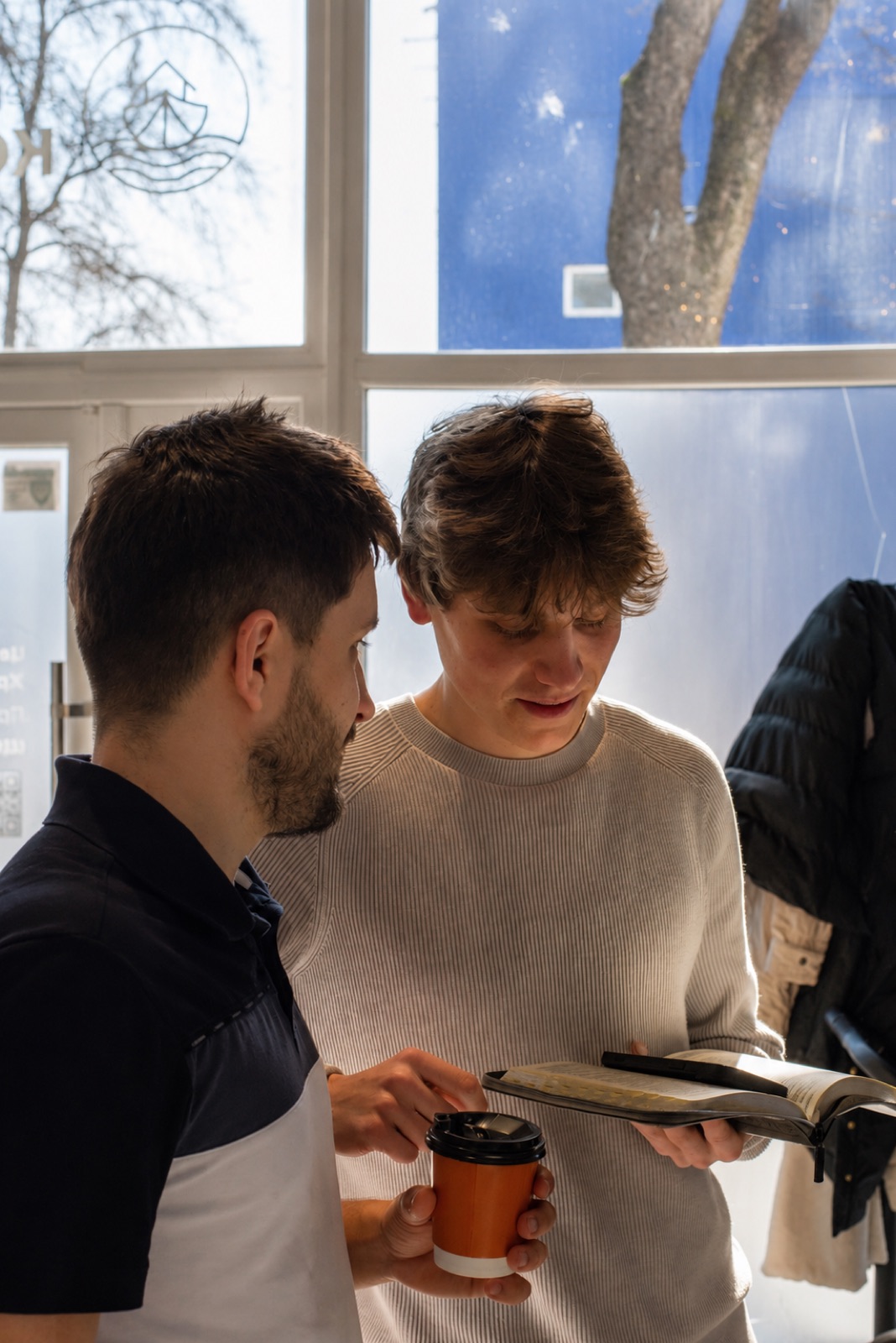 Two men with coffee looking at a Bible by the window